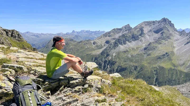 Mann sitzt neben seinem Rucksack und blickt auf die Berge. | © Frank Eichmann